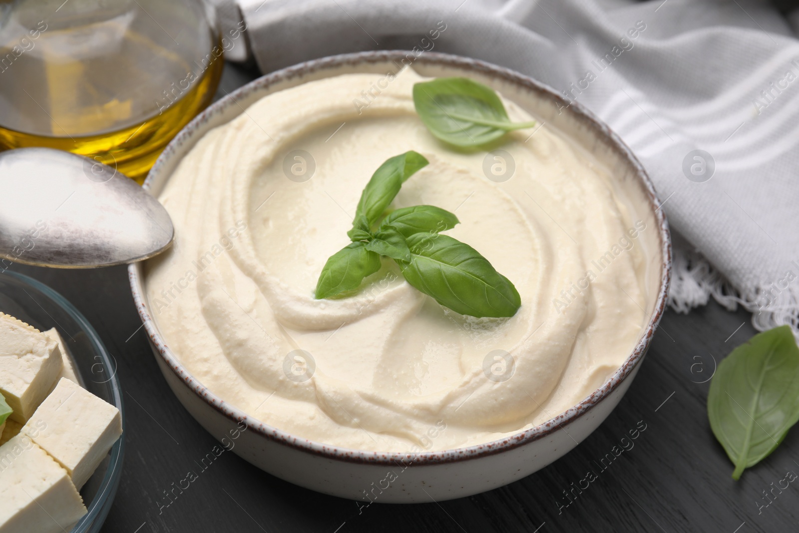Photo of Delicious tofu sauce and basil leaves in bowl on grey table, closeup