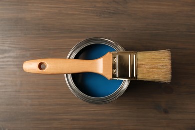 Photo of Can of blue paint and brush on wooden background, top view