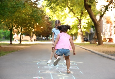 Photo of Little children playing hopscotch drawn with colorful chalk on asphalt