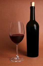 Photo of Glass and bottle of red wine on brown background