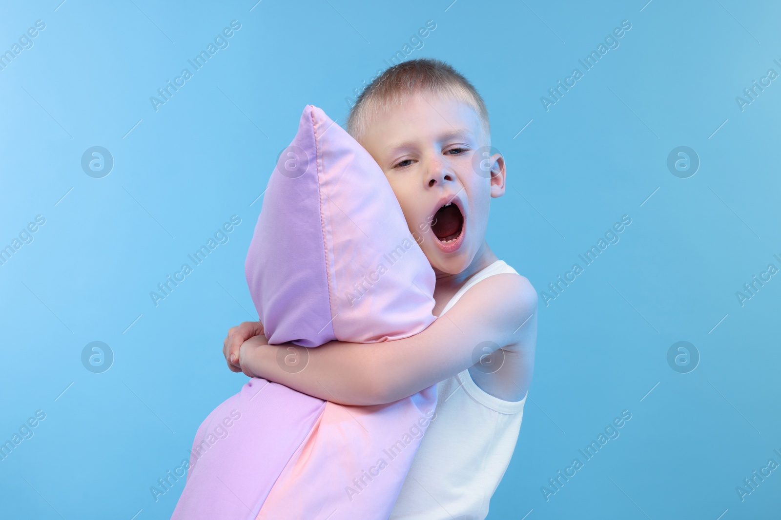 Photo of Sleepy boy with pillow yawning on light blue background. Insomnia problem