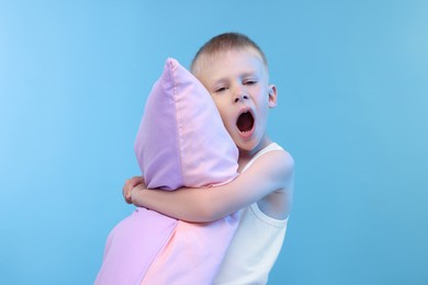 Photo of Sleepy boy with pillow yawning on light blue background. Insomnia problem