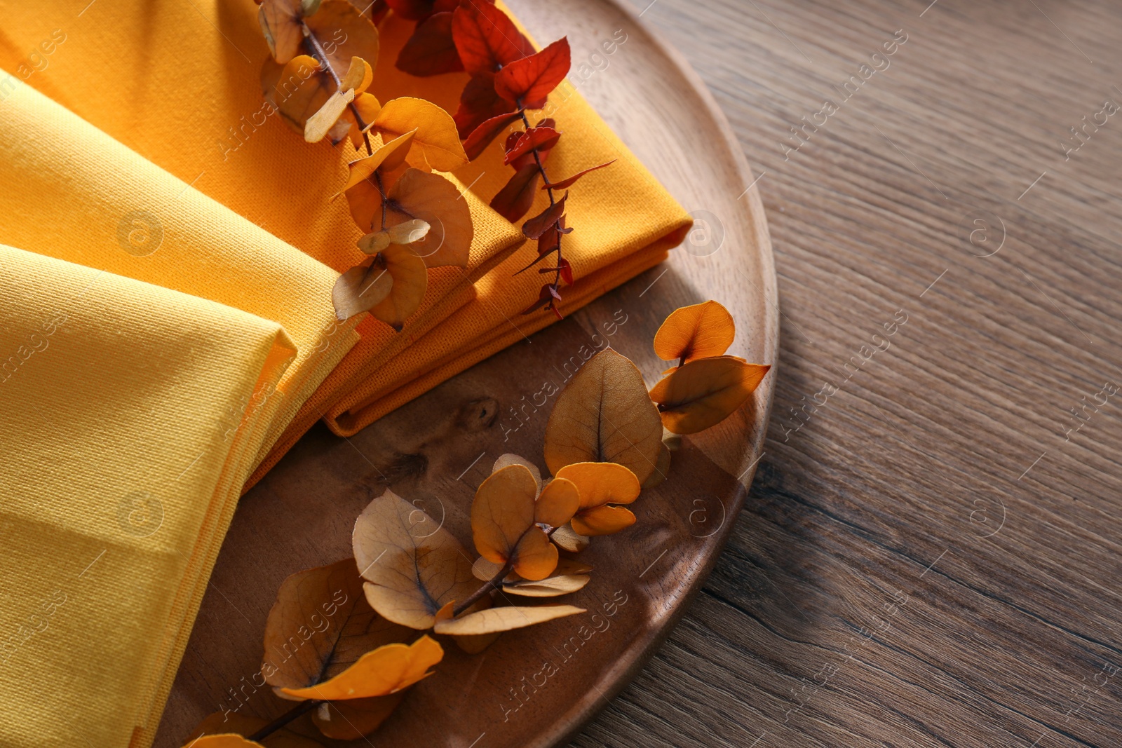 Photo of Tray with different kitchen napkins and decorative dry leaves on wooden table, top view. Space for text