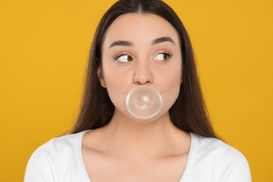 Beautiful young woman blowing bubble gum on yellow background