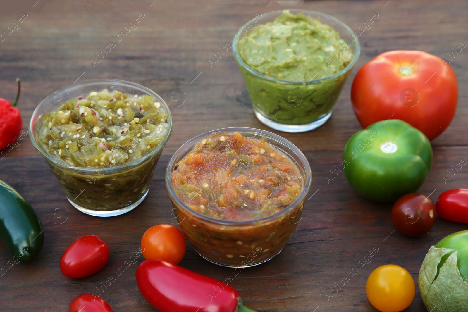 Photo of Tasty salsa sauces and ingredients on wooden table