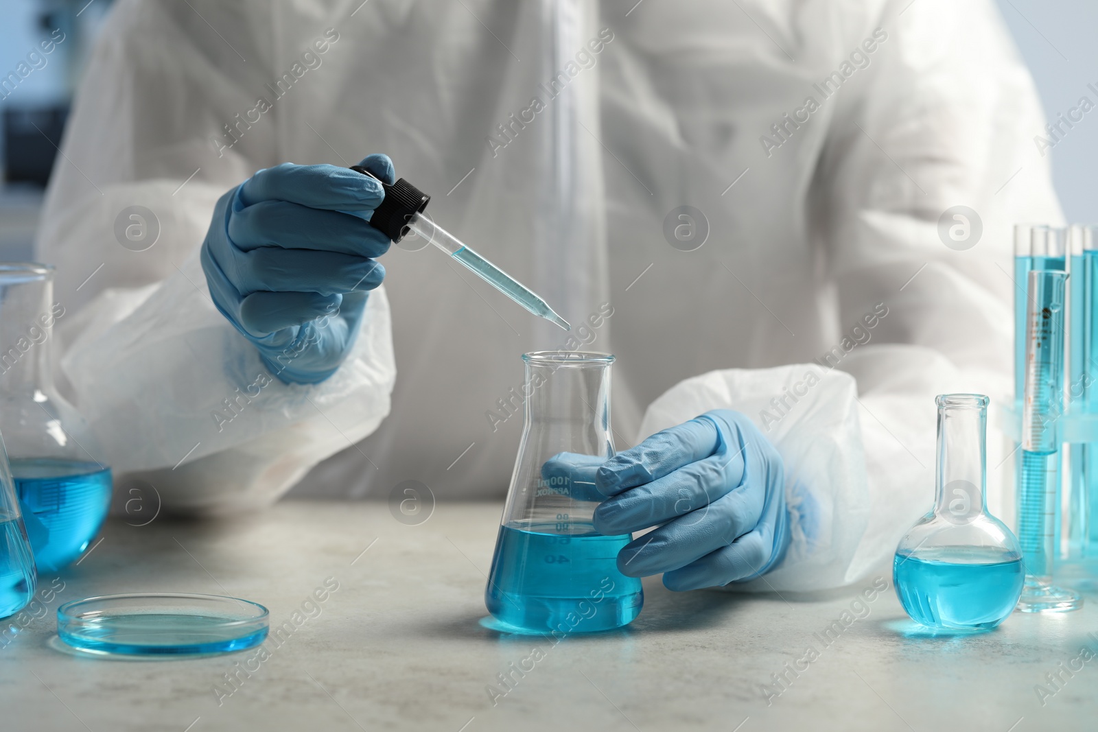 Photo of Scientist dripping liquid from pipette into beaker at white table in laboratory, closeup