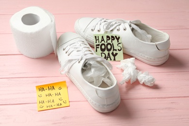 Shoes with toilet paper and Happy Fools' Day note on pink wooden background