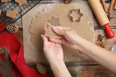 Woman holding gingerbread star over wooden table, top view. Homemade Christmas cookies