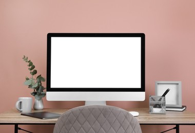 Modern computer with blank screen on desk near pink wall, space for design. Comfortable workplace