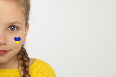 Photo of Little girl with drawing of Ukrainian flag on face in heart shape against white background, closeup. Space for text