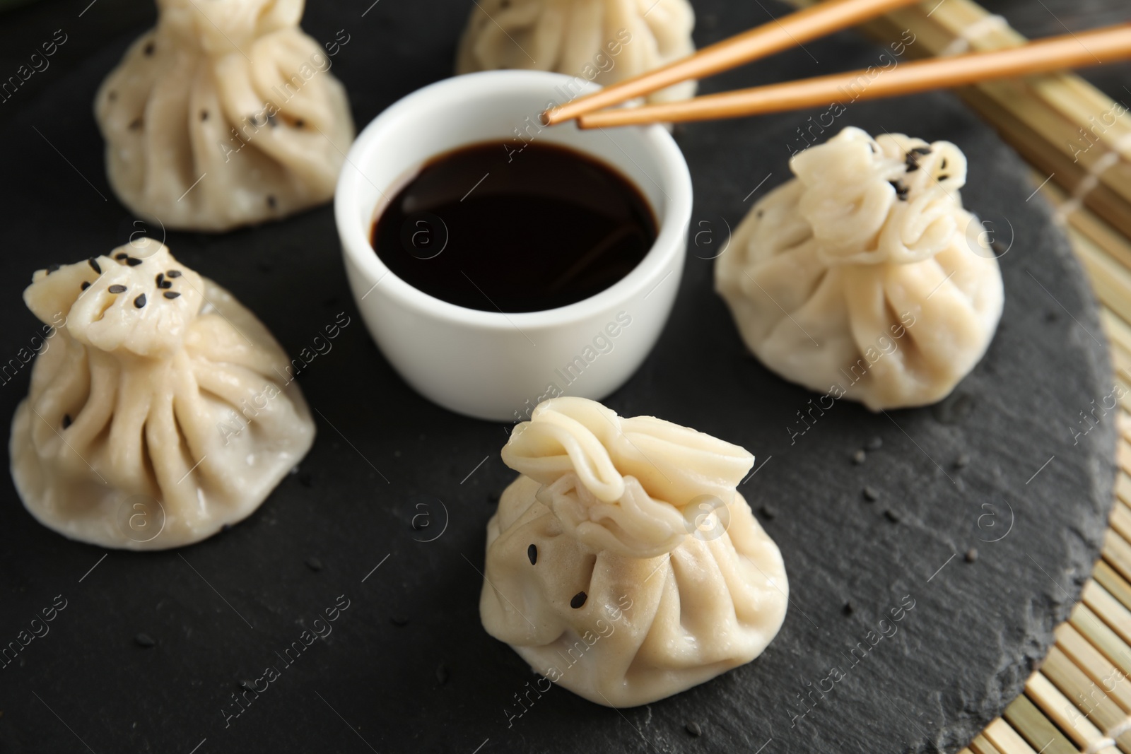 Photo of Slate plate with tasty baozi dumplings, chopsticks and soy sauce on table, closeup