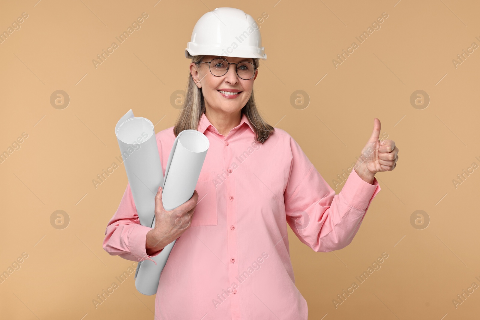 Photo of Architect in hard hat with drafts showing thumbs up on beige background