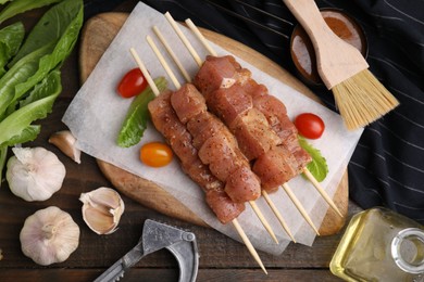 Photo of Skewers with cut raw marinated meat on wooden table, flat lay