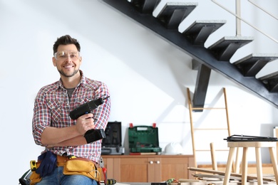 Handsome working man with electric screwdriver indoors, space for text. Home repair