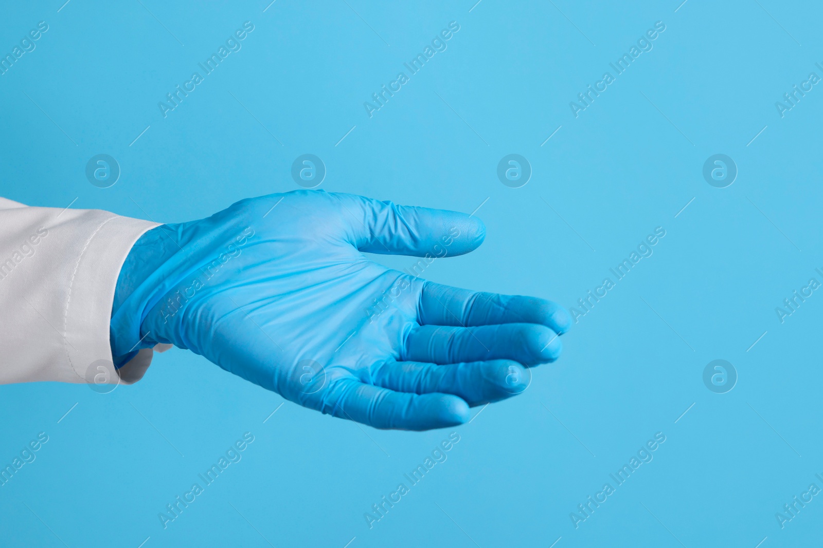 Photo of Doctor wearing medical glove holding something on light blue background, closeup