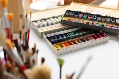 Photo of Different brushes near colorful paints on white table. Artist's workplace