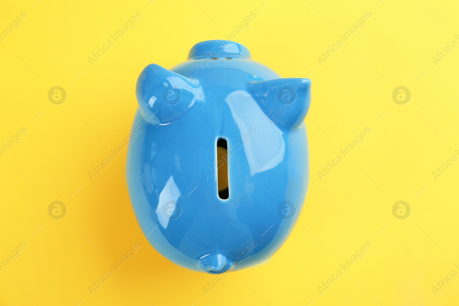 Photo of Blue piggy bank on yellow background, top view