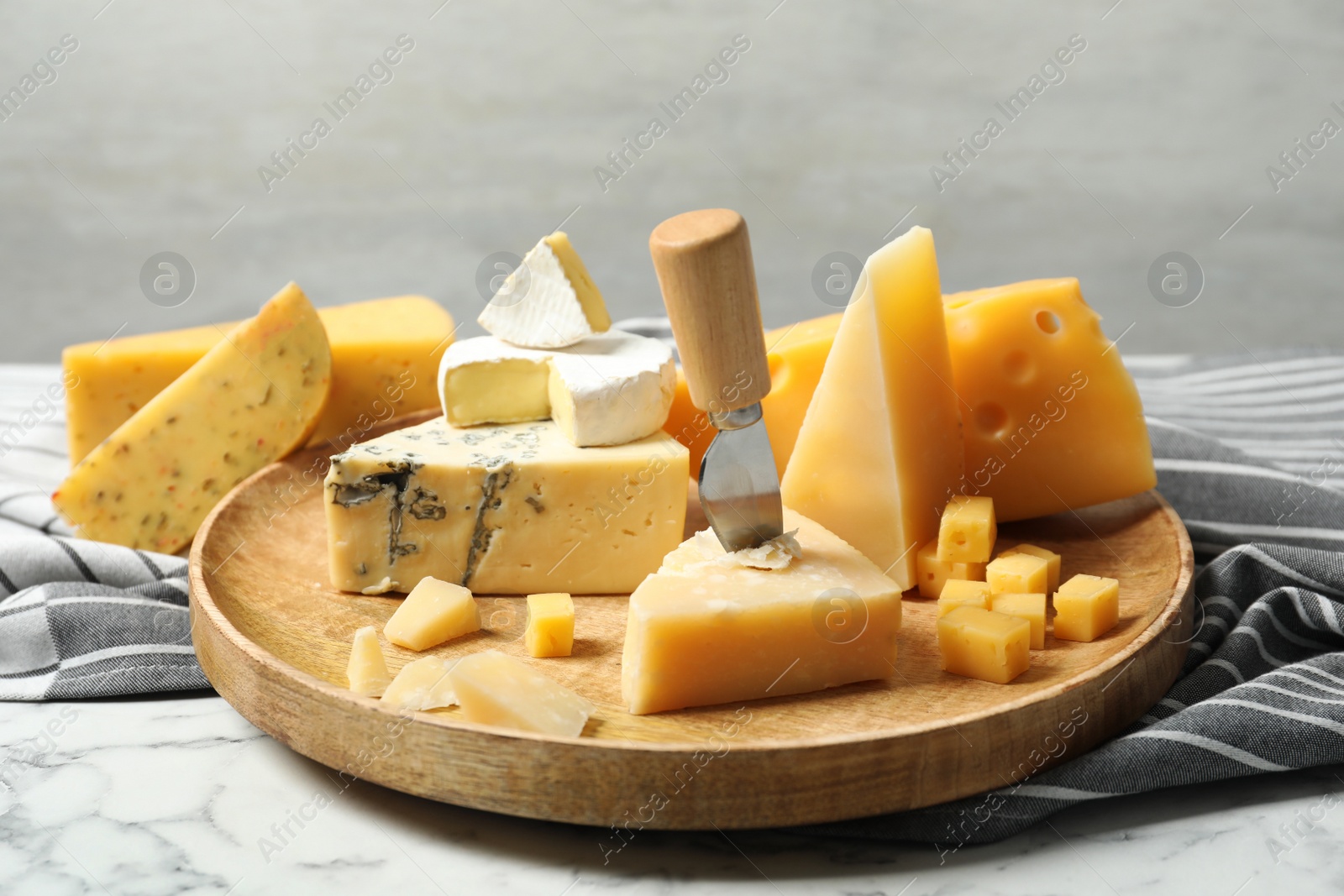 Photo of Wooden plate with different types of delicious cheese on marble table against light background