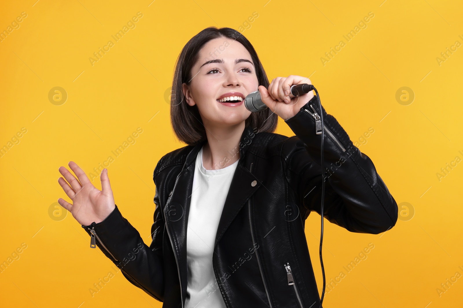 Photo of Beautiful young woman with microphone singing on yellow background