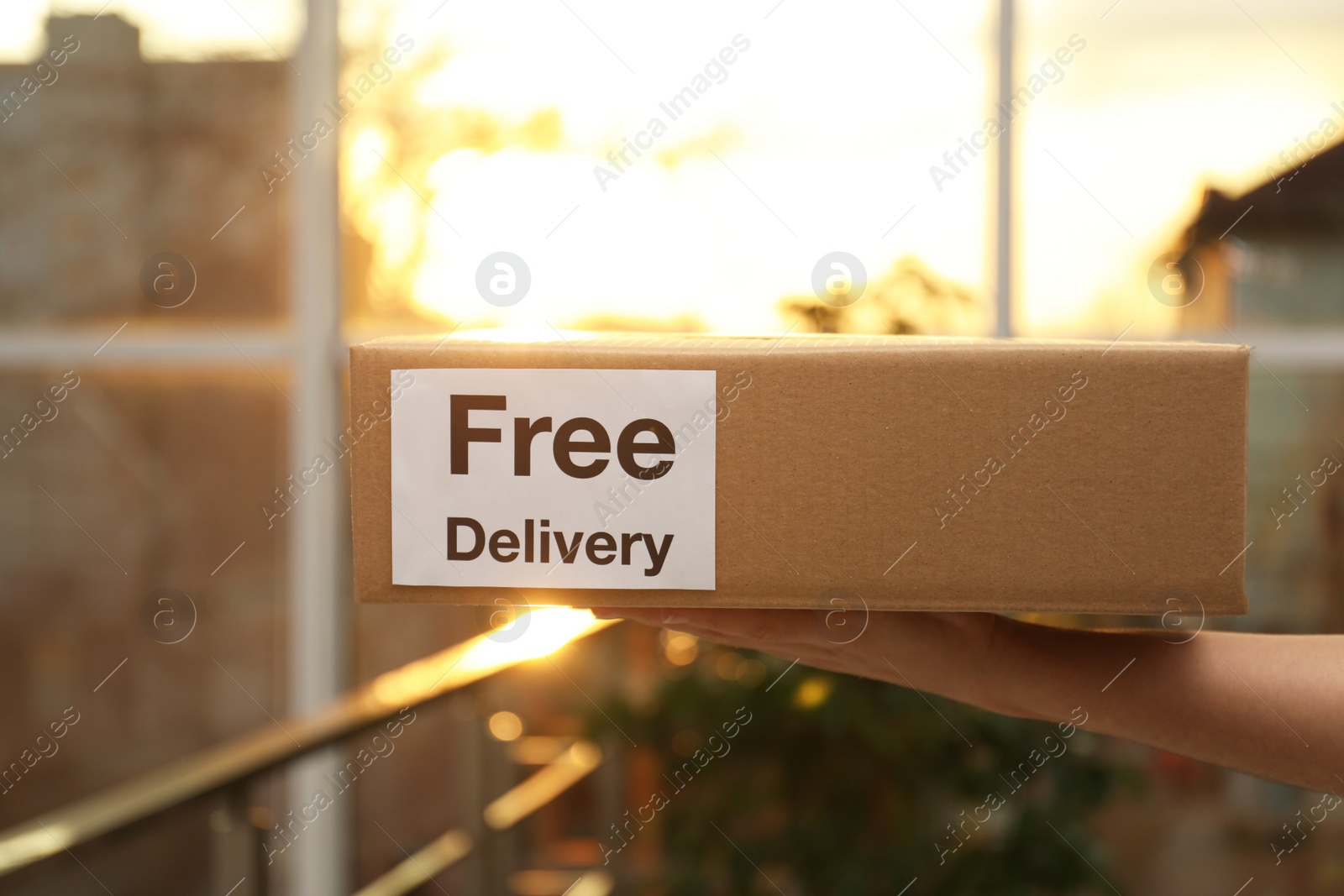 Photo of Courier holding parcel with sticker Free Delivery indoors, closeup