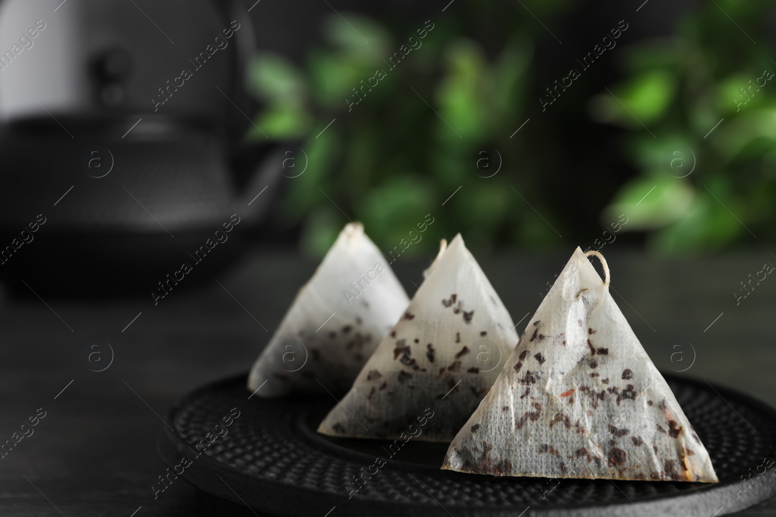 Photo of Saucer with used pyramid tea bags on black table, closeup. Space for text