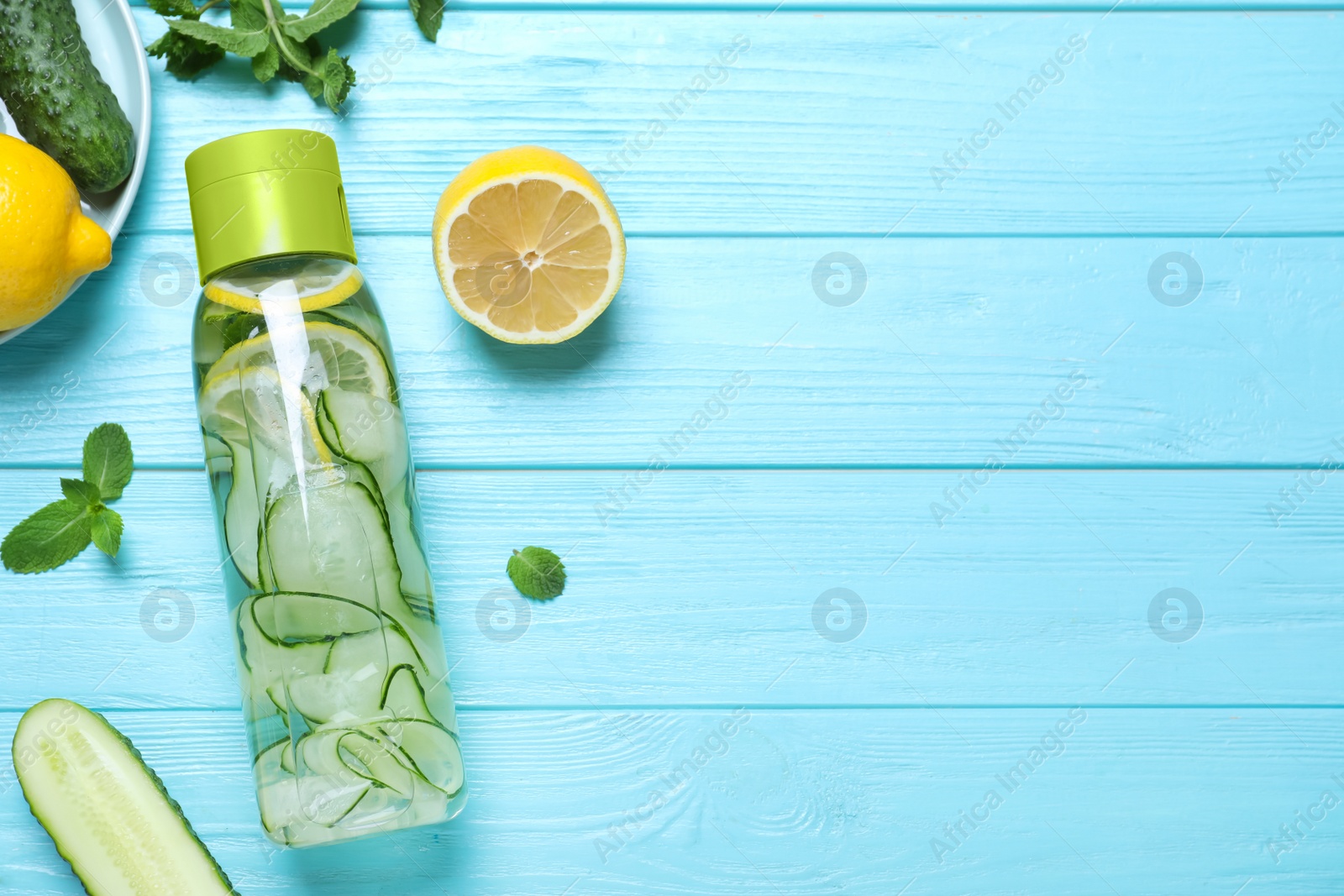 Photo of Bottle of refreshing water with cucumber, lemon and mint on light blue wooden table, flat lay. Space for text