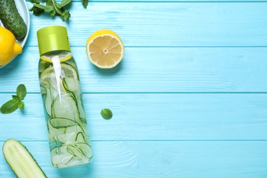 Bottle of refreshing water with cucumber, lemon and mint on light blue wooden table, flat lay. Space for text