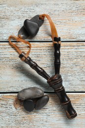 Photo of Black slingshot with stones on old light blue wooden table, flat lay