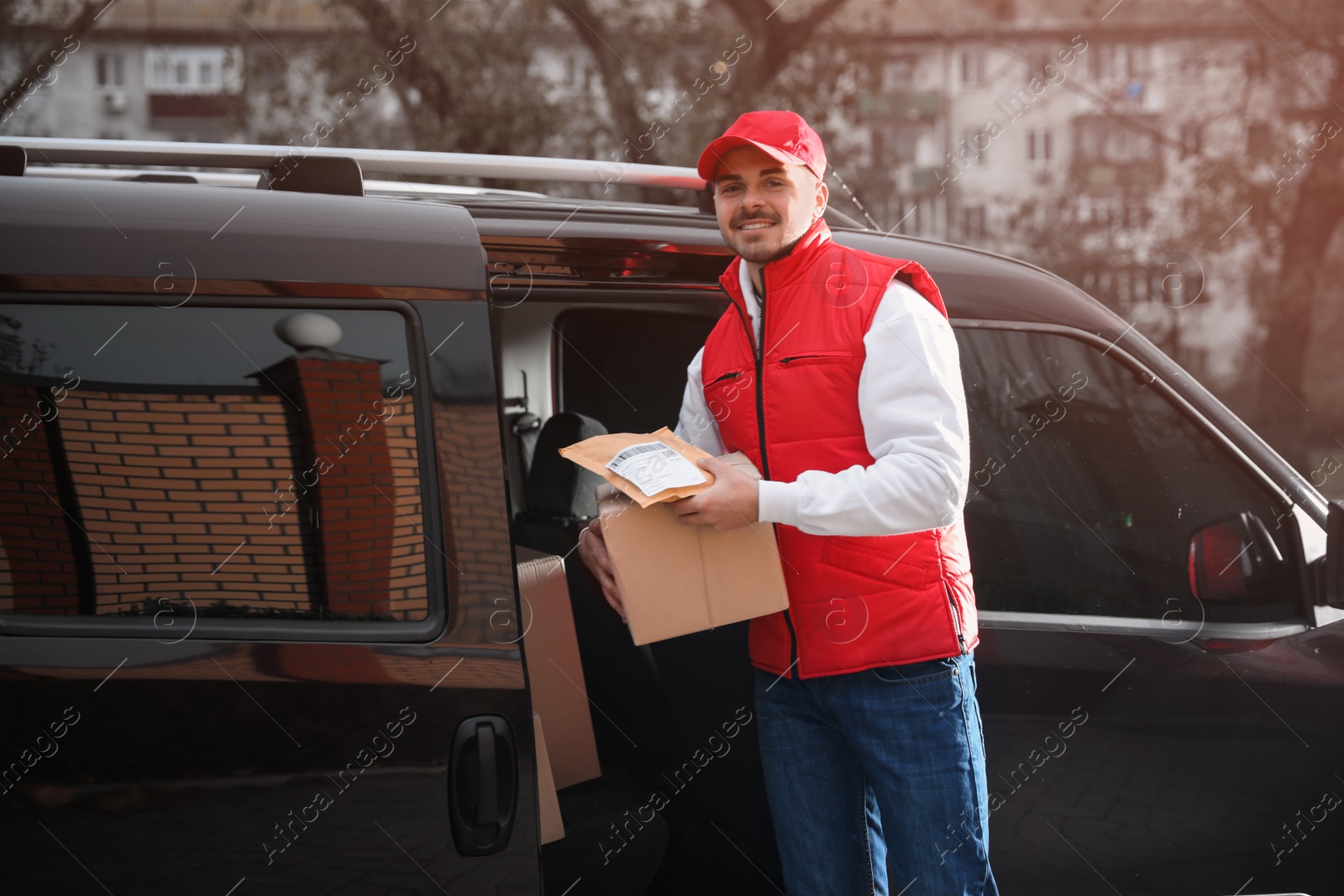 Photo of Deliveryman in uniform with parcels near van outdoors