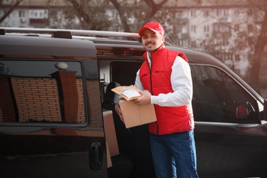 Photo of Deliveryman in uniform with parcels near van outdoors