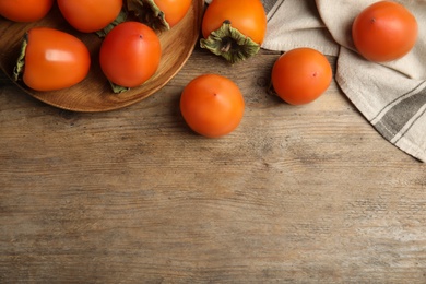 Photo of Tasty ripe persimmons on wooden table, flat lay. Space for text