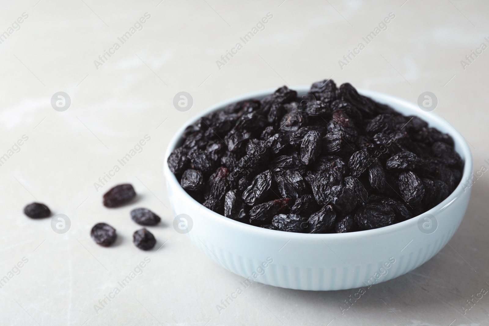 Photo of Bowl with raisins on grey table, space for text. Dried fruit as healthy snack