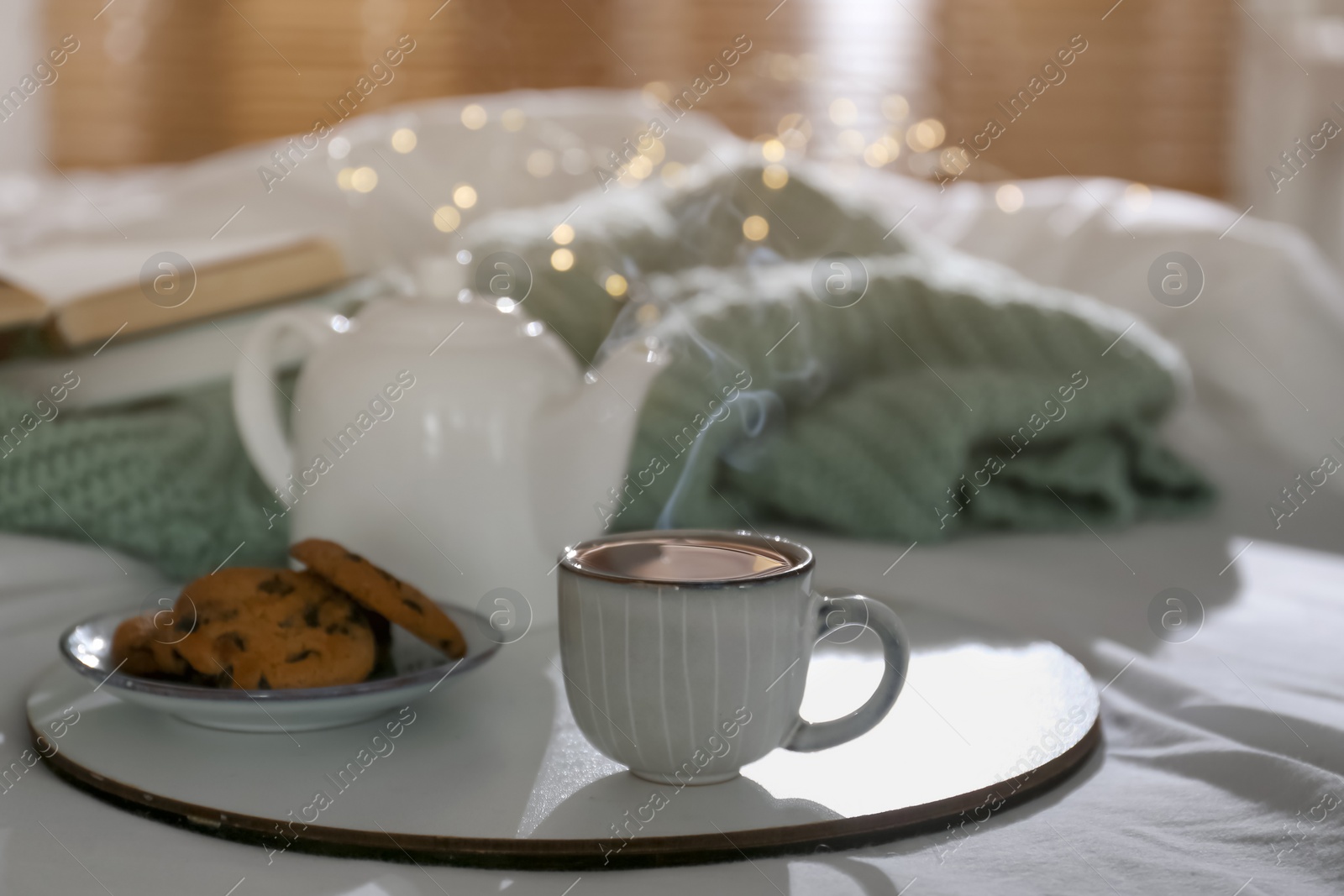 Photo of Tray with cup of hot tea, cookies and teapot on bed indoors