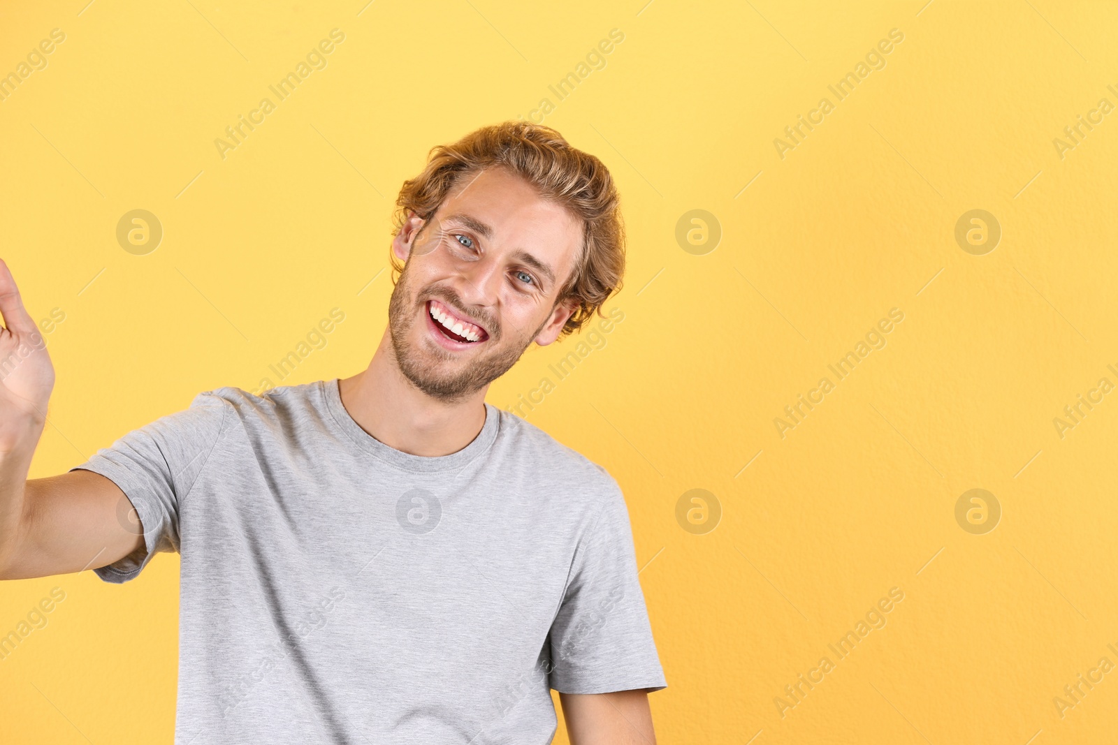 Photo of Handsome young man laughing and taking selfie on color background