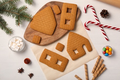 Photo of Parts of gingerbread house, ingredients and fir tree branch on white wooden table, flat lay