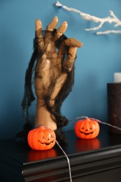 Photo of Jack-o'-lantern lights and wooden hand on black fireplace near blue wall