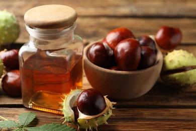 Chestnuts and jar of essential oil on wooden table