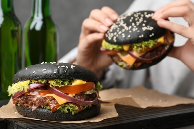 Tasty burger with black buns and woman eating on background