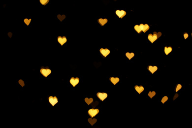 Blurred view of heart shaped lights on black background. Bokeh effect