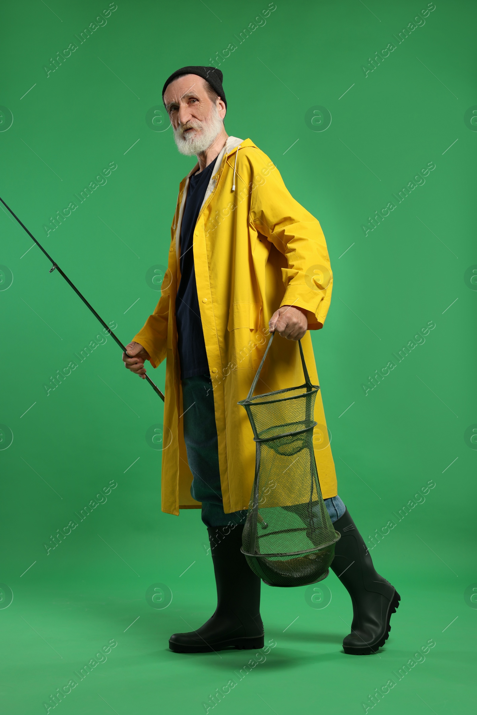 Photo of Fisherman holding rod and fishing net with catch on green background