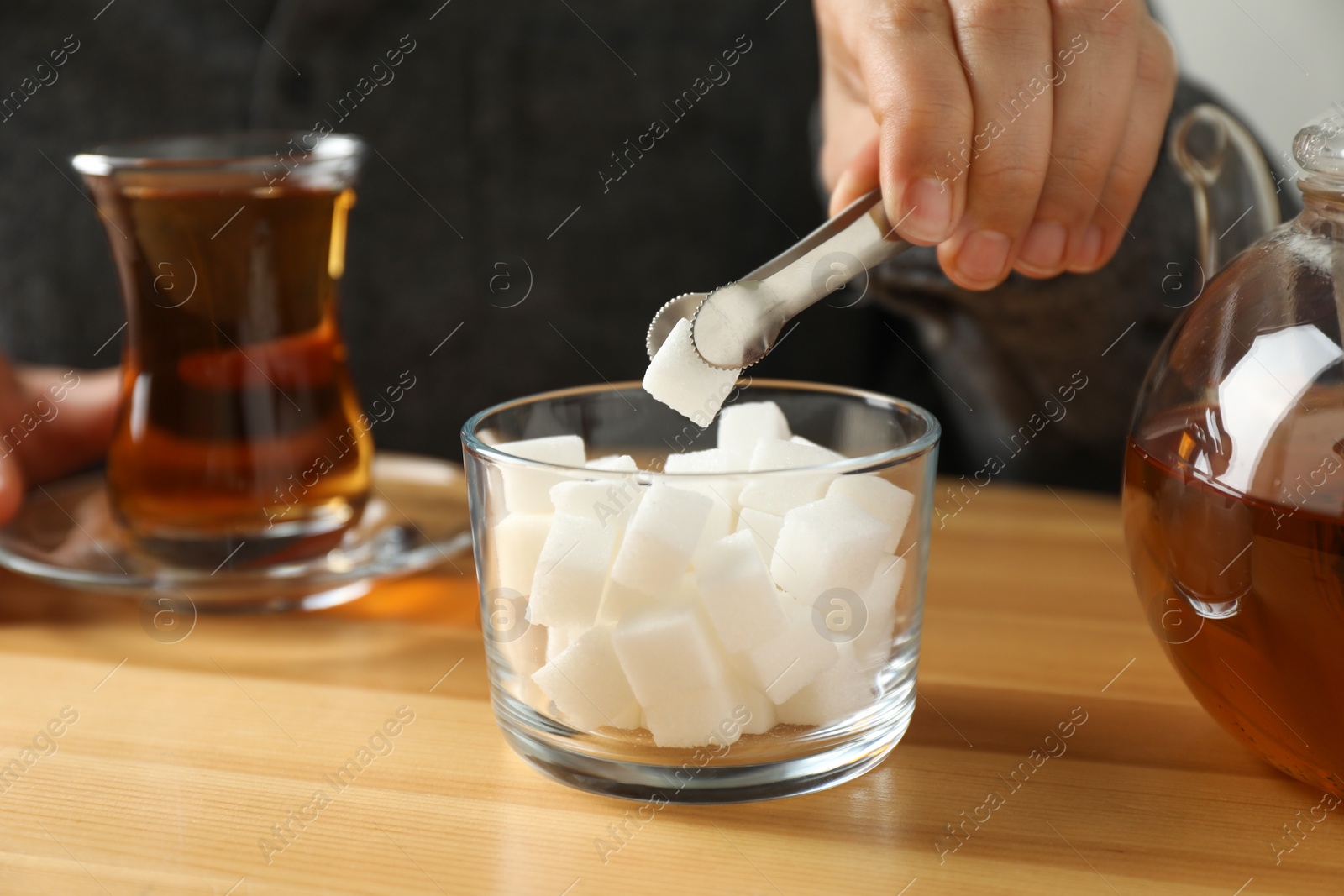 Photo of Woman adding sugar cube into aromatic tea at wooden table, closeup