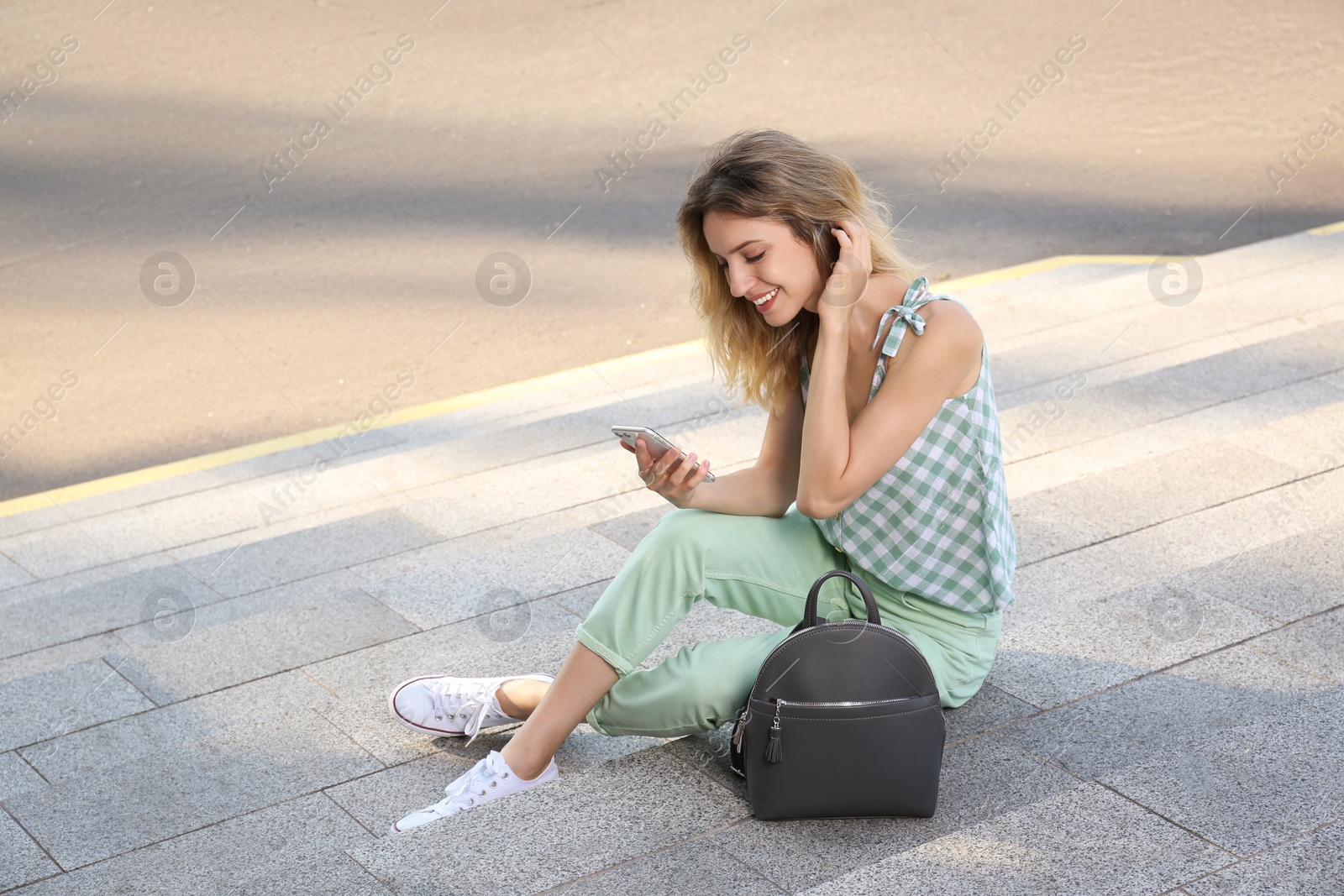 Photo of Young woman with stylish backpack and smartphone on stairs outdoors