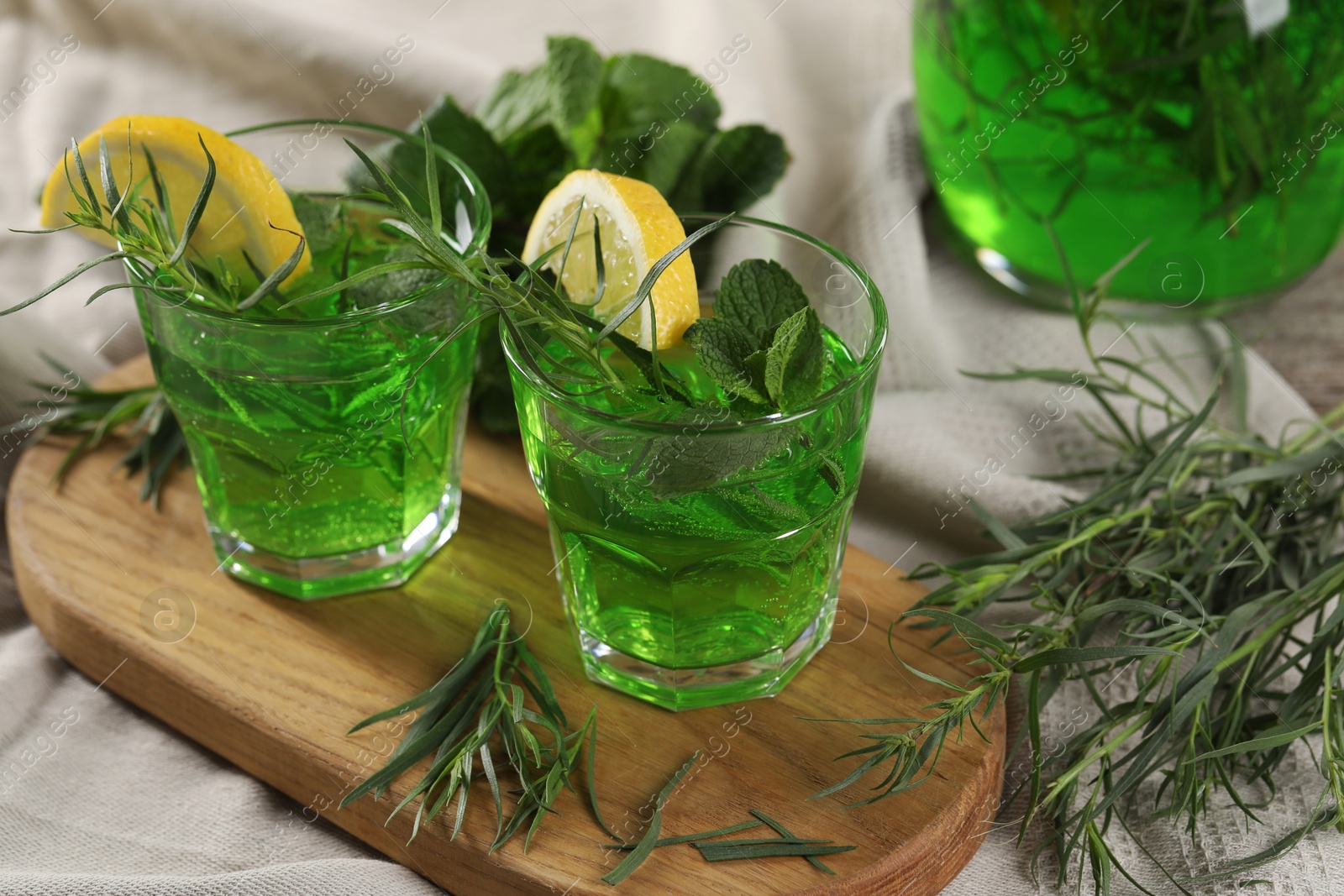 Photo of Glasses of refreshing tarragon drink with lemon slices on tablecloth