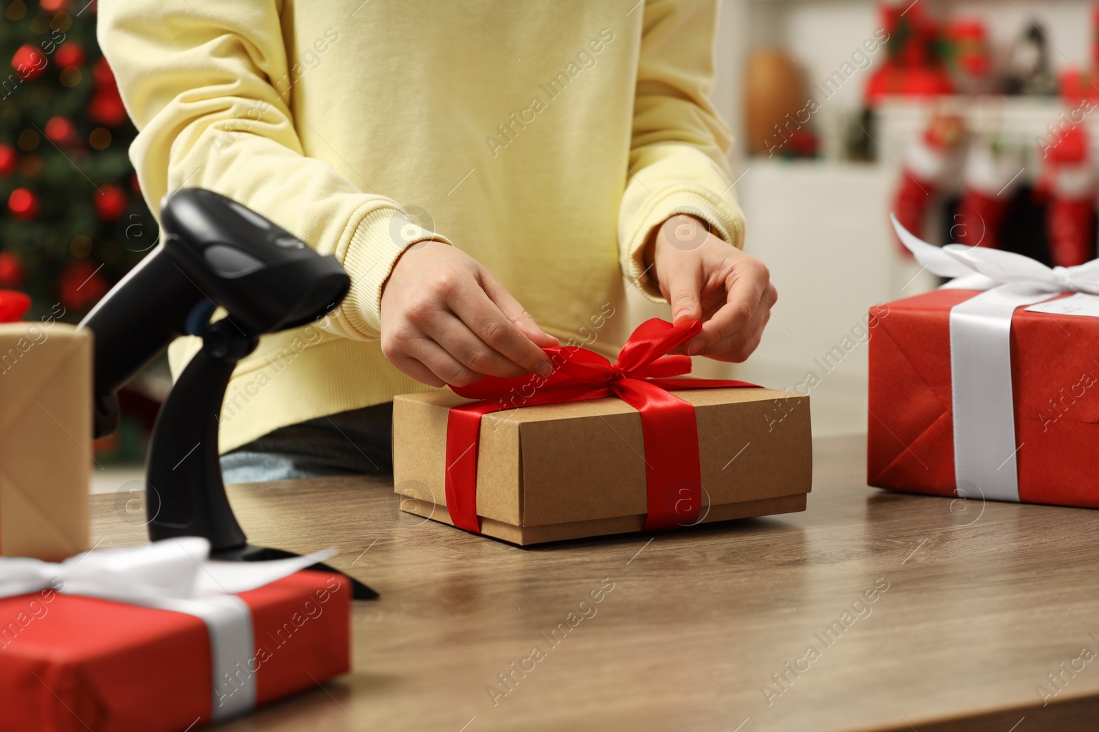 Photo of Woman preparing Christmas gift box at wooden table in post office, closeup