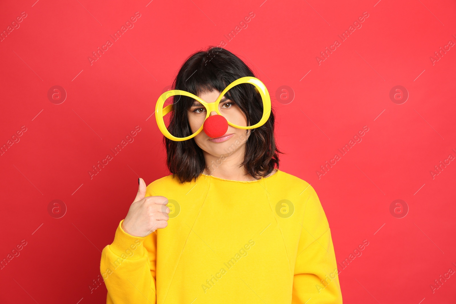 Photo of Emotional woman with large glasses and clown nose on red background. April fool's day