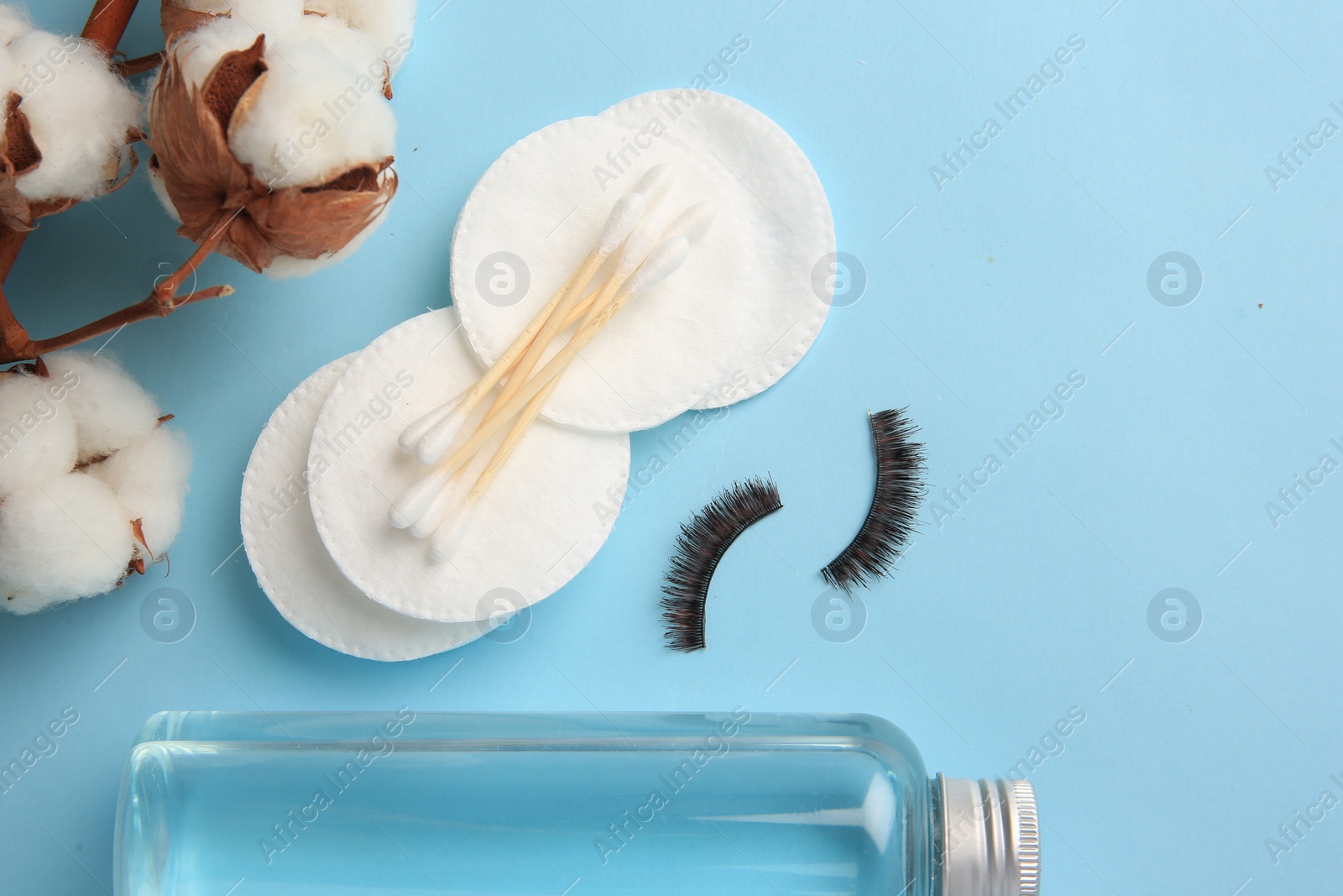 Photo of Bottle of makeup remover, cotton flowers, pads, swabs and false eyelashes on light blue background, flat lay. Space for text