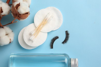 Bottle of makeup remover, cotton flowers, pads, swabs and false eyelashes on light blue background, flat lay. Space for text