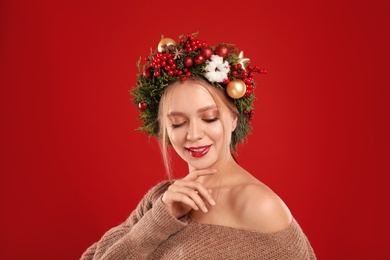 Photo of Beautiful young woman wearing Christmas wreath on red background