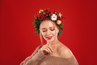 Beautiful young woman wearing Christmas wreath on red background