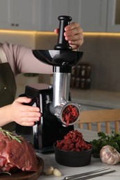Photo of Woman making beef mince with electric meat grinder at white marble table in kitchen, closeup